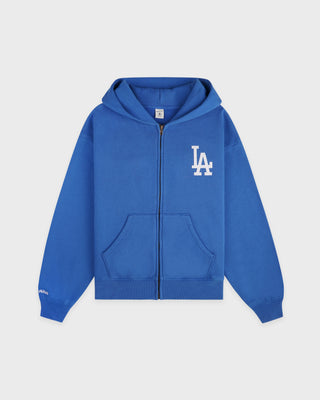 LA Serif Zip Hoodie in Team Blue/White, featuring a white LA logo on the left chest, front pockets, and a zip closure. Crafted from 100% cotton with an oversized fit and displayed laid flat on a white background.