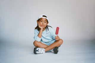Child sitting on the floor holding a popsicle against a plain background
