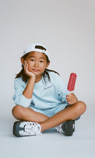 Child sitting on the floor holding a popsicle against a plain background