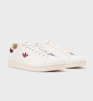 The Stan Smith - White/Merlot sneakers showcase a vintage-inspired design with white uppers and striking merlot Adidas logo and accents, reminiscent of the classic Stan Smith silhouette, set against a plain white background.