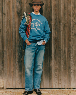 Person wearing a blue sweatshirt with text and graphics, standing against a wooden wall.
