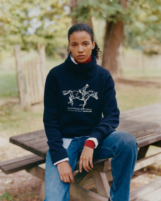 Person wearing a navy blue sweater with a graphic design, sitting on a wooden bench outdoors.