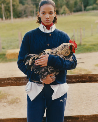 Person wearing a navy sweater and white shirt holding a rooster outdoors.