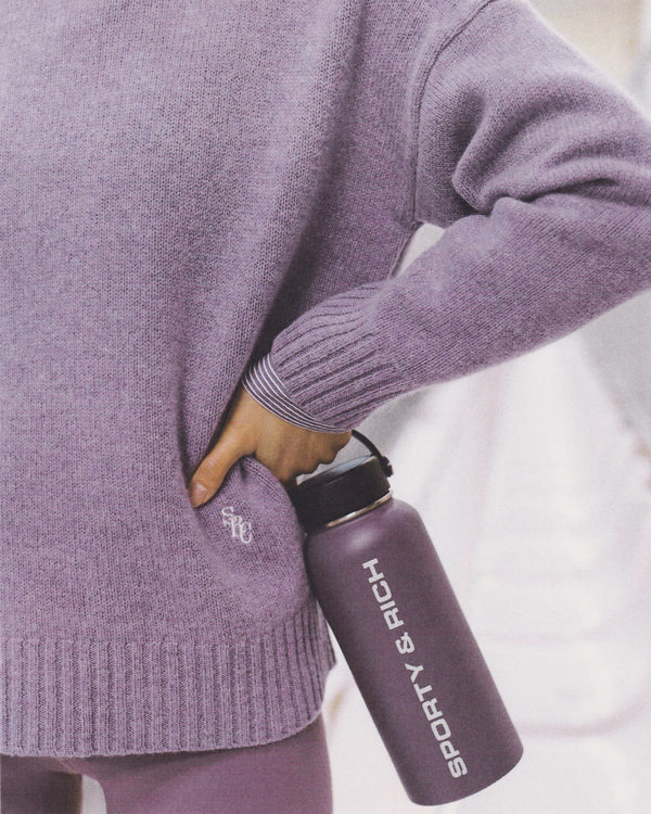 Person in an eggplant SRC Turtleneck holding a matching “Sporty & Rich” water bottle against their side.