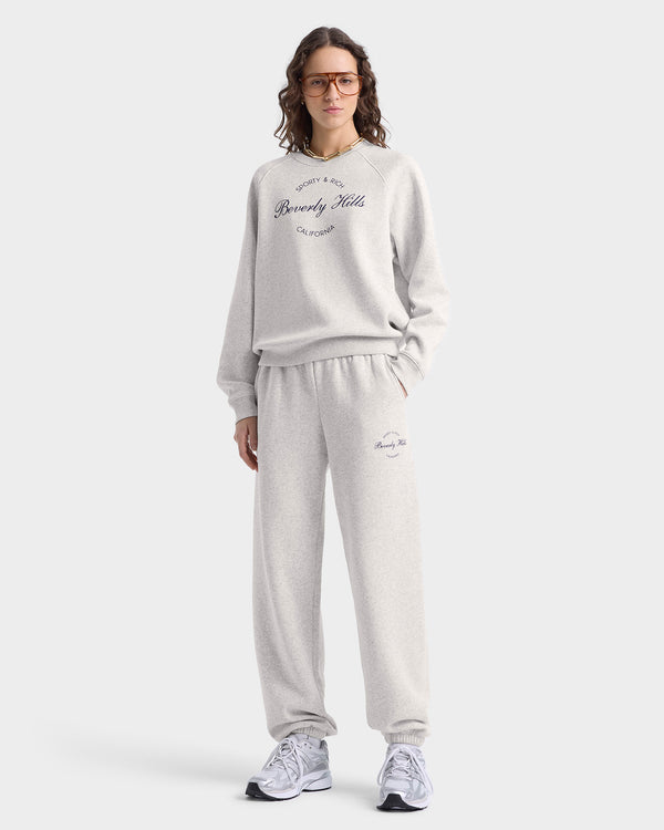 A person in Beverly Script Soft Sweatpant - Heather Gray/Navy, paired with a gray cotton sweatshirt, sneakers, and glasses, stands casually.