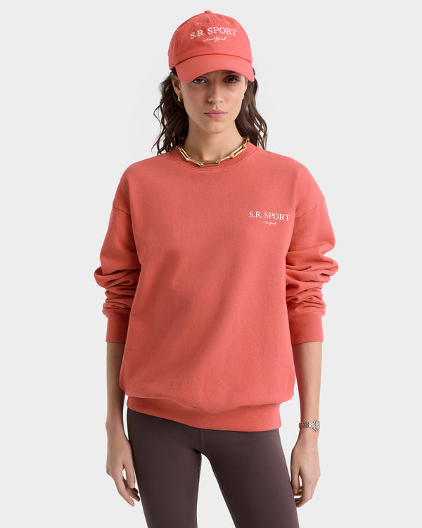 Someone in the Wimbledon Crewneck - Desert Rose/White, featuring the S.R. Sport logo and made in Los Angeles from USA-grown cotton, pairs it with a matching coral hat and brown leggings against a neutral background.