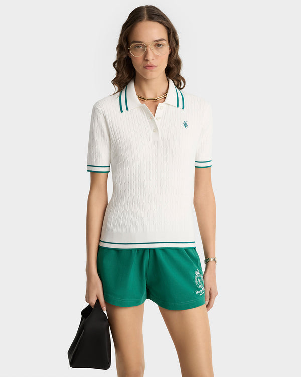 Woman wearing a white polo shirt with green accents and green shorts on a white background