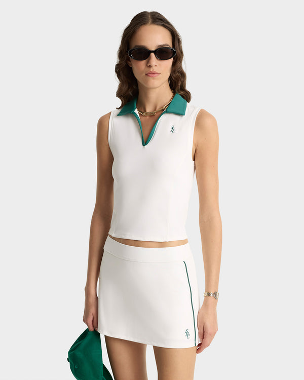 Woman wearing a white sleeveless top and skirt with green accents on a white background