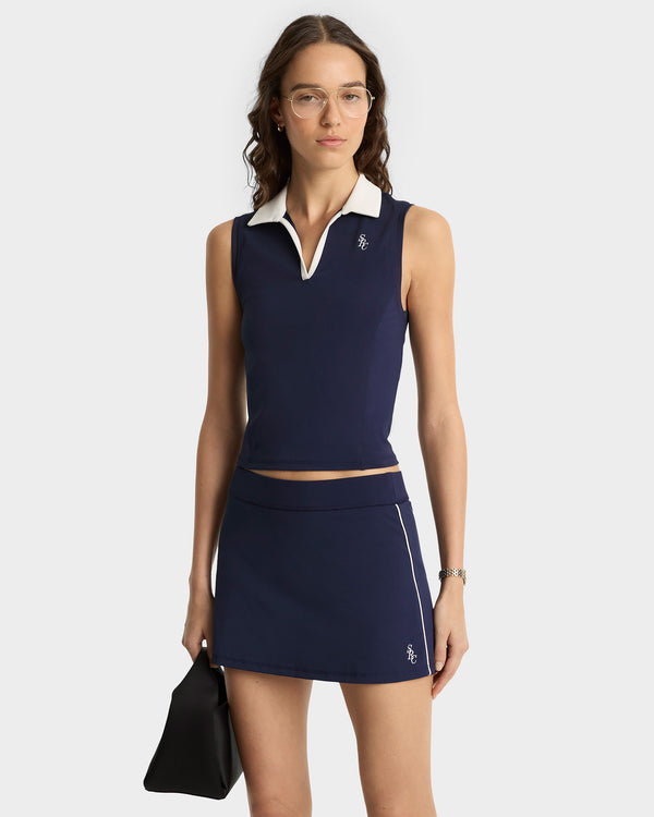 Woman wearing a navy blue sleeveless top and skirt with white accents on a white background