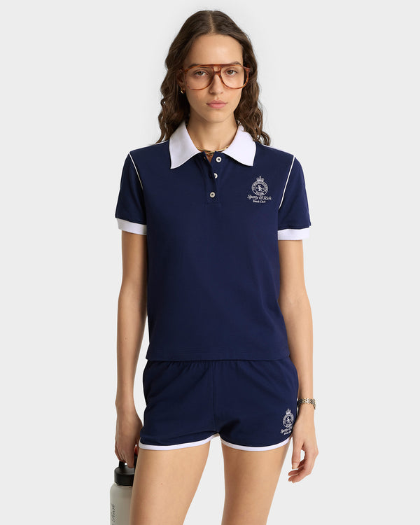 Woman wearing a navy blue polo shirt and shorts set with a logo on a white background