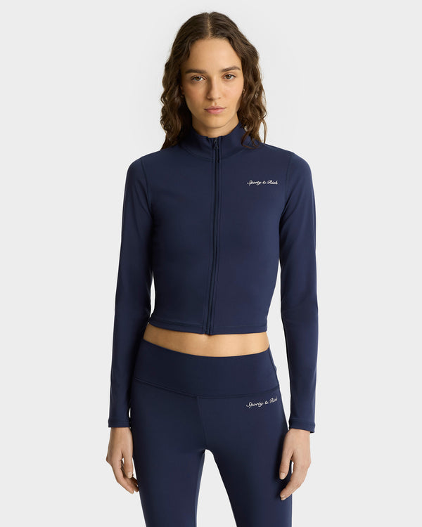 A woman stands against a plain background in the Syracuse Sports Jacket - Navy/White with a zipped closure and matching high-waisted leggings. The comfortable set is ideal for both active and casual wear.
