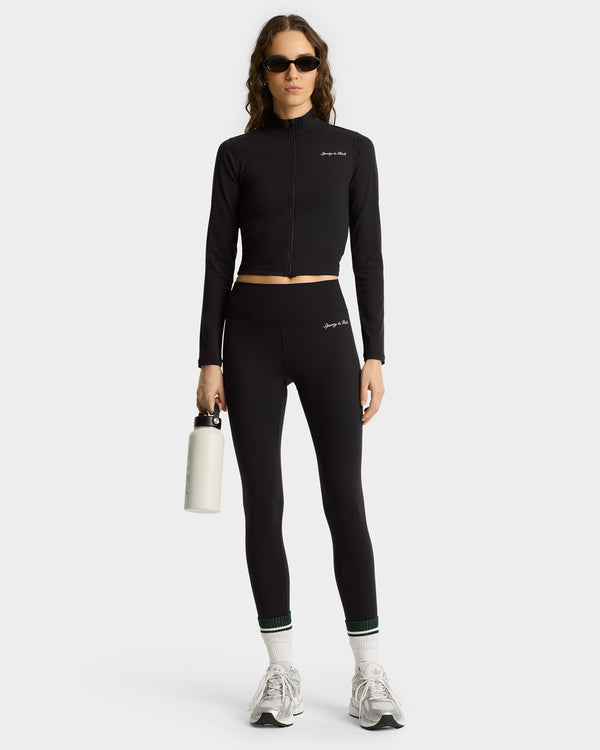 Wearing Syracuse Leggings - Black/White, a woman in sunglasses stands confidently in sneakers and socks, holding a white water bottle.