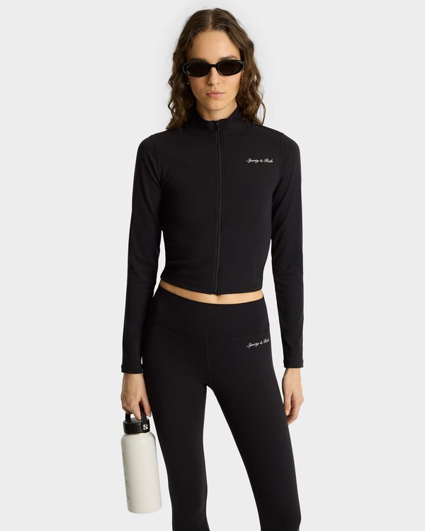 Woman in a Syracuse Sports Jacket - Black/White with comfortable fabric and zipped closure, wearing sunglasses and holding a white water bottle against a plain background.