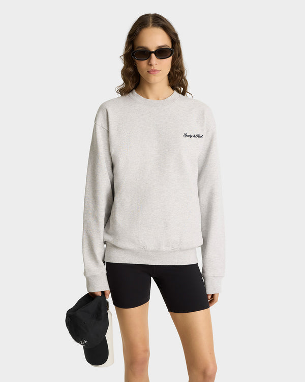 Woman in sunglasses wearing the Syracuse Embroidered Crewneck in Heather Gray/Navy with black shorts, holding a black cap against a plain background.
