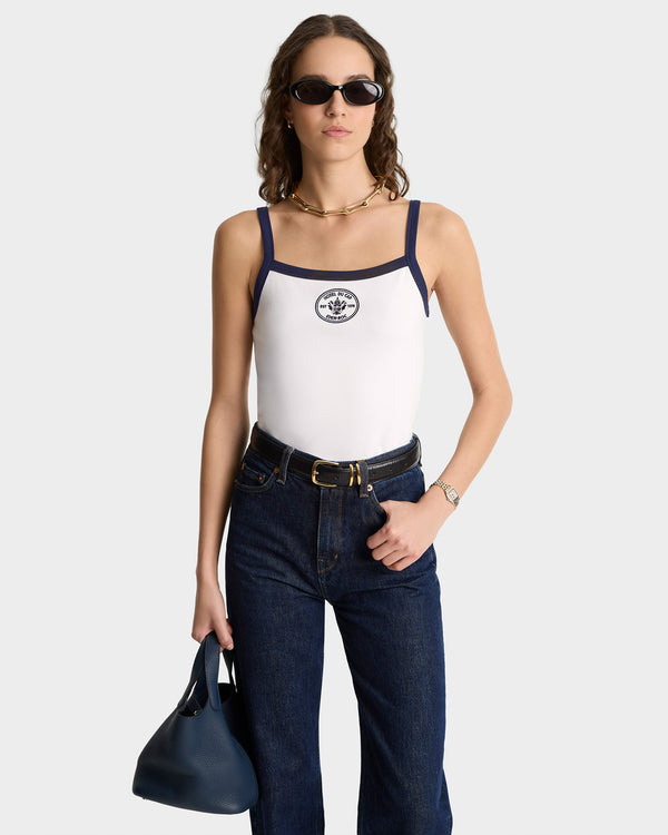 Woman wearing sunglasses, jeans, and holding a navy handbag, styled with the Eden Crest Embroidered Pique Tank in White/Navy featuring blue trim.