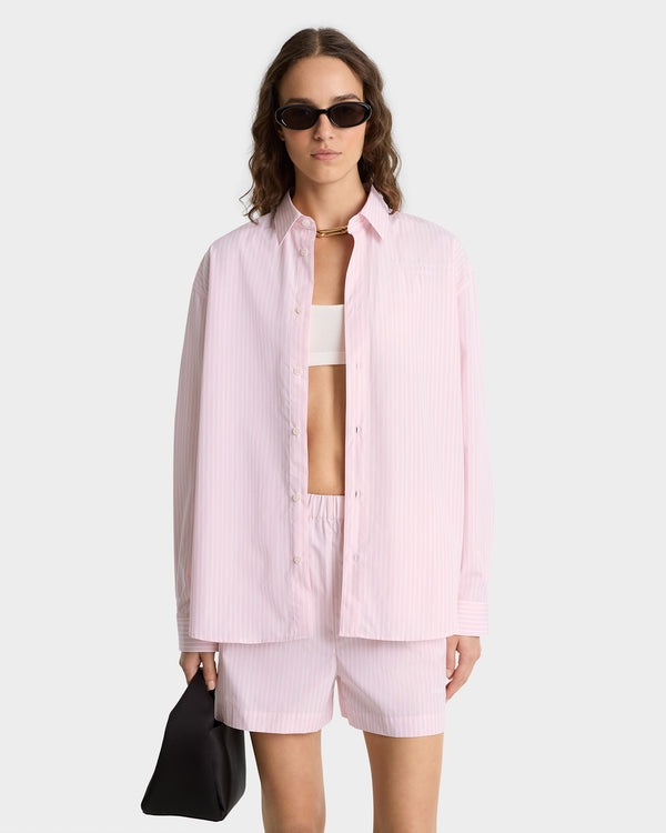 Woman in sunglasses wears the Eden Script Oversized Shirt in pink and white thin stripe—cotton poplin, relaxed fit, made in Portugal—for an effortlessly stylish look.