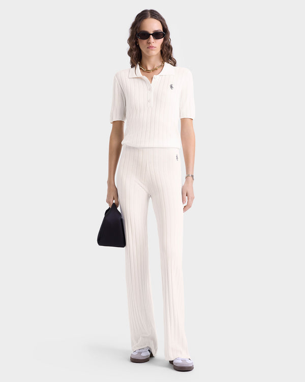 Woman in SRC Ribbed Trousers - Ecru/Navy with elastic waistband, white ribbed knit polo, sunglasses, and black handbag, standing against a white background.