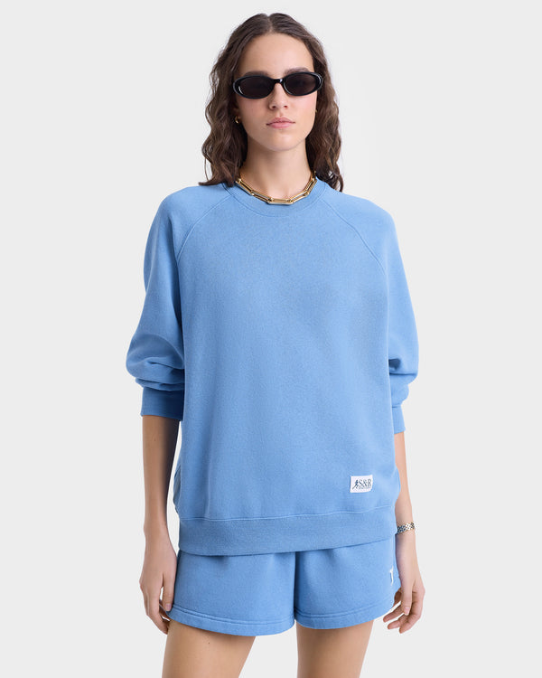 Woman in sunglasses wears the SR Runner Soft Crewneck in Juniper/White and matching shorts, standing against a plain background.