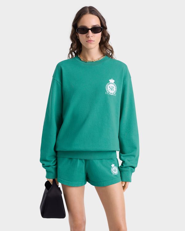 Woman wearing the Royal Club Crewneck in Spring Green/White, matching shorts, sunglasses, a gold necklace, and holding a black handbag.