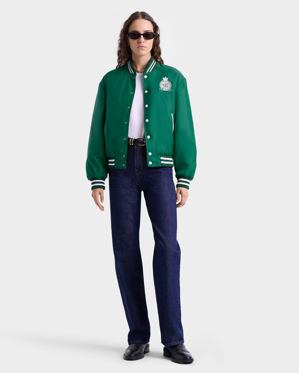 A person in sunglasses wears the Royal Club Nylon Varsity Jacket in Spring Green/White, paired with a white shirt, blue jeans, and black shoes.