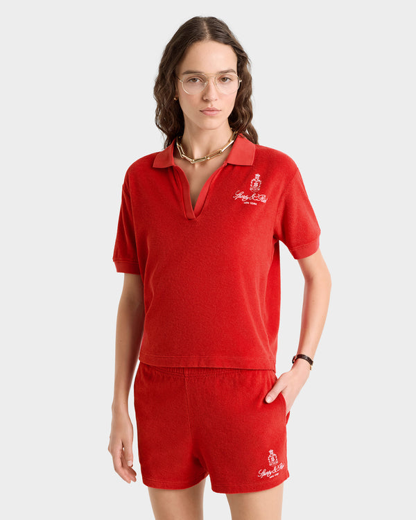A woman wears the Vendome Terry Polo in Fire Red/White with matching shorts, glasses, and a necklace.