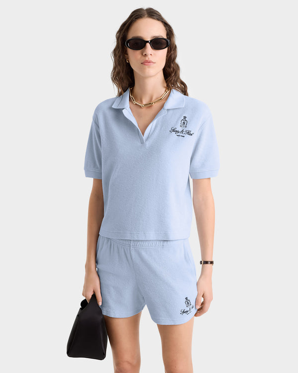 A woman wearing the Vendome Terry Polo - Ciel/Navy and shorts, made from 100% cotton in Portugal.