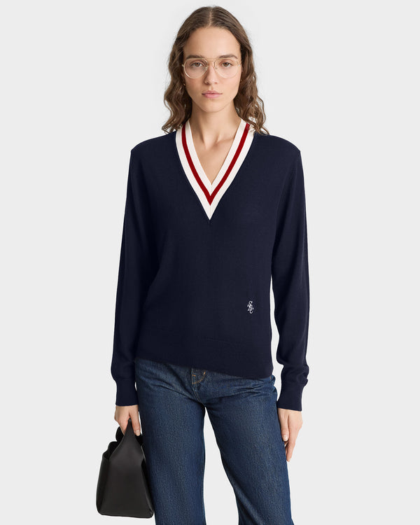 Woman in glasses wears the SRC Minimalist V-Neck Sweater in Navy/Ecru/Ruby with blue jeans and holds a black bag.