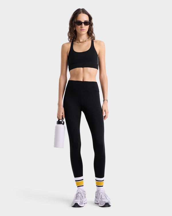Model wearing black high-waisted leggings with white side stripes and supportive seaming, paired with matching sports bra.
