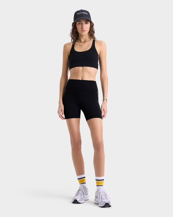 Model wearing high-waisted black athletic shorts with white side stripes, featuring a wide waistband and supportive seaming, paired with matching sports bra.
