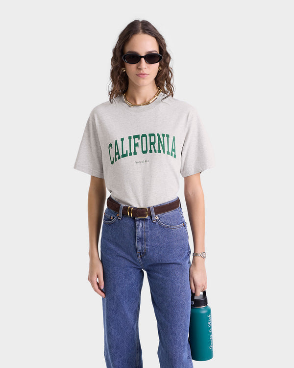 Close up of model wearing heather grey T-shirt with 'CALIFORNIA' in large green letters across the chest and smaller 'Sporty & Rich' text below, featuring a crew neckline.