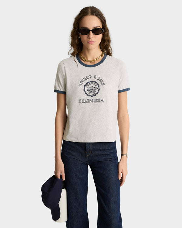 Woman in sunglasses wearing the California Emblem Soft Ringer Tee in heather gray/navy, made in Portugal, with jeans. She holds a cap and a white bag.