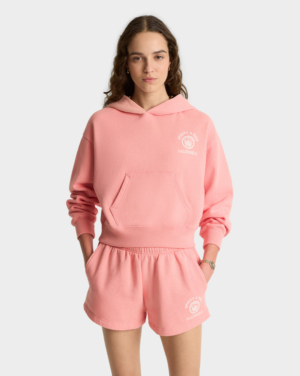 Woman in a California Emblem Soft Cropped Hoodie - Carnation/White, made in Portugal, standing against a plain white background.
