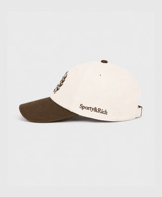 A two-tone baseball cap with an off-white crown and a brown curved brim, featuring a brown embroidered crest logo on the front.