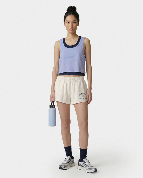 Person wearing a light blue tank top and white shorts, holding a water bottle on a white background