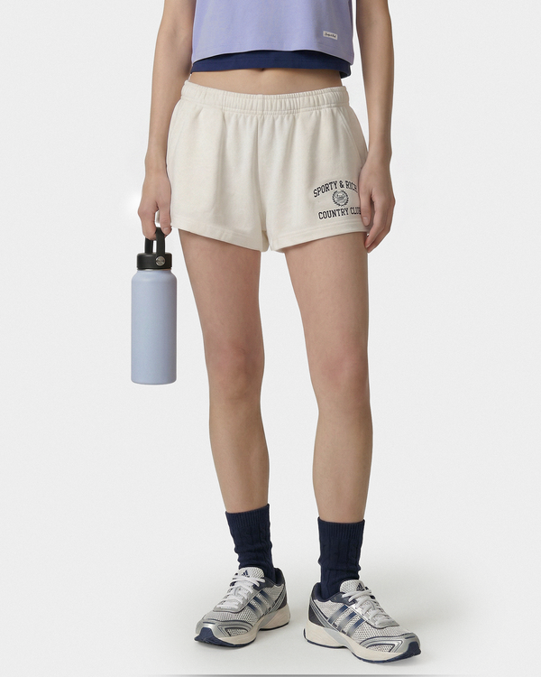 Person wearing cream shorts with text, holding a water bottle on a white background