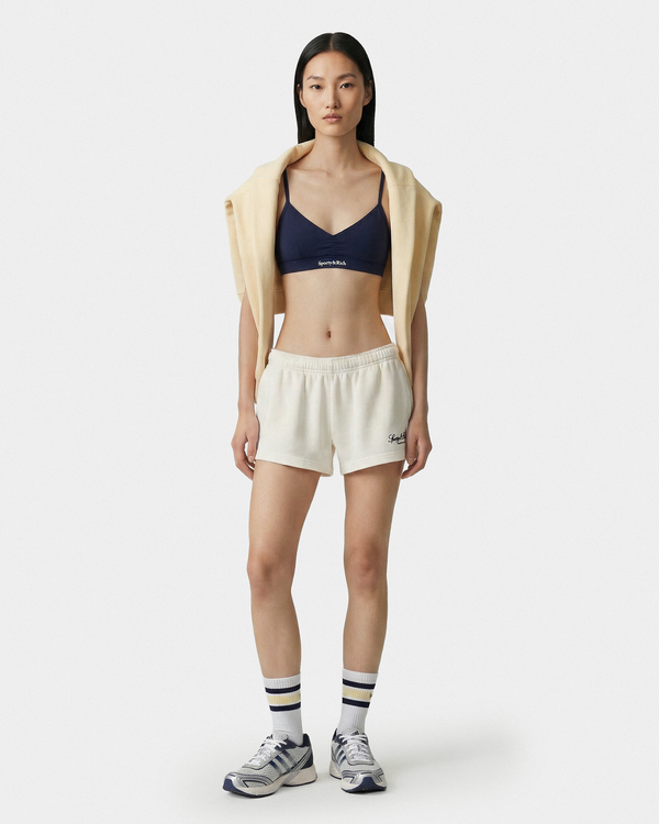 Woman wearing a navy sports bra and beige shorts on a white background