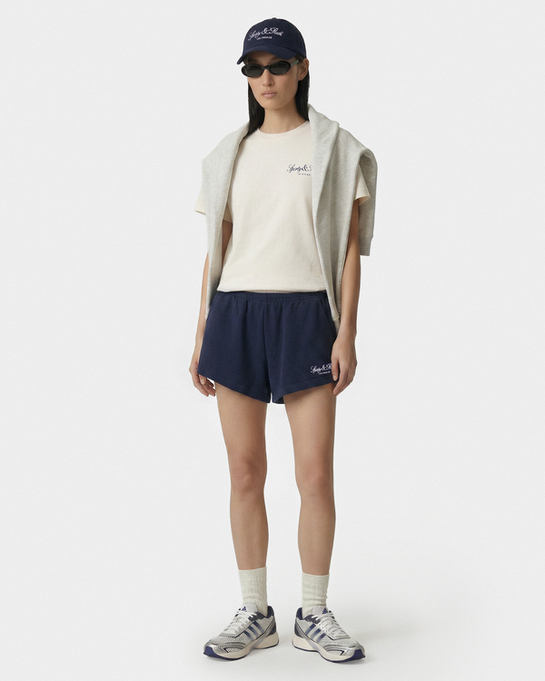 Person wearing a white t-shirt, navy shorts, and a cap on a white background