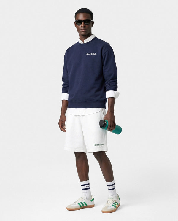 Man wearing a navy sweater, white shorts, and green sneakers on a white background