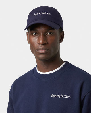 Person wearing a navy cap and sweatshirt with 'Sporty&Rich' branding on a white background