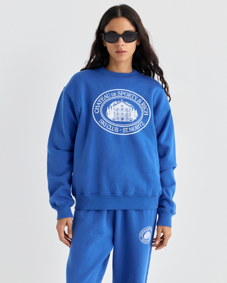 Vibrant blue Emmett Chateau Crewneck with a white circular logo featuring a ski lodge graphic.