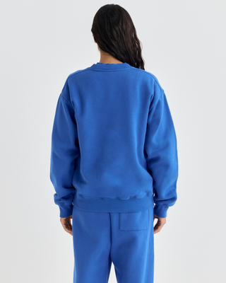 Vibrant blue Emmett Chateau Crewneck with a white circular logo featuring a ski lodge graphic.