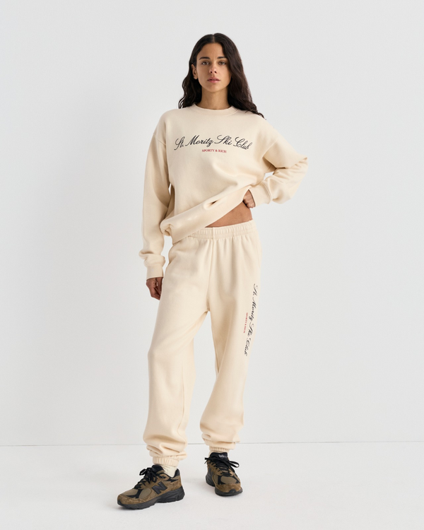 Woman wearing a cream-colored Sporty & Rich sweatshirt and matching Brianno Ski Club Jogger in a classic fit.