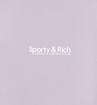 White Sporty & Rich RUNNING AND HEALTH CLUB text on a light purple background, perfect for pairing with the Club Logo Legging - Faded Lilac or high waisted leggings.