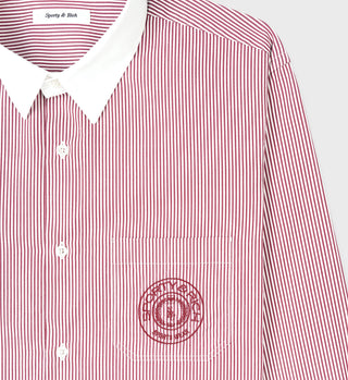 The Connecticut Crest Striped Shirt - Merlot features red and white cotton poplin stripes, a white collar, an embroidered chest logo, and is crafted in Portugal for timeless style and quality.