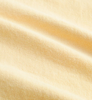 Close-up of soft, light yellow Health Is Wealth T-Shirt - Almond/H2O with gentle folds and fine texture, crafted from USA grown cotton.