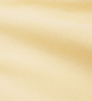 Close-up of the NY Racquet Club T-Shirt in Almond/Navy, showing soft light yellow fabric with fine horizontal texture and gentle folds, crafted from 100% USA-grown cotton.