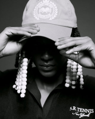 A person adjusts their embroidered cap while wearing an SR Tennis Longsleeve Terry Polo in Navy/White. The monochrome ensemble exudes elegance and comfort with its 100% cotton design.