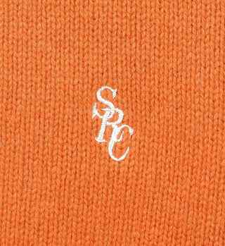 Close-up of turmeric SRC Wool Crewneck featuring orange lambswool knit and white embroidered overlapping SRC letters at the center.