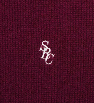 Close-up of the SRC Turtleneck - Merlot, featuring maroon knit 100% Lambswool fabric with white embroidered overlapping SPC letters at the center.